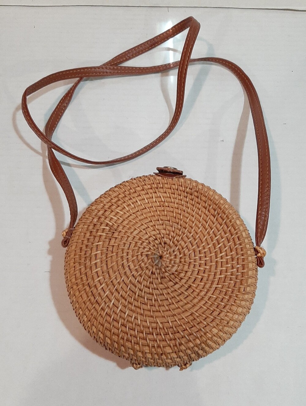 Round, handwoven rattan crossbody bag featuring a brown leather strap